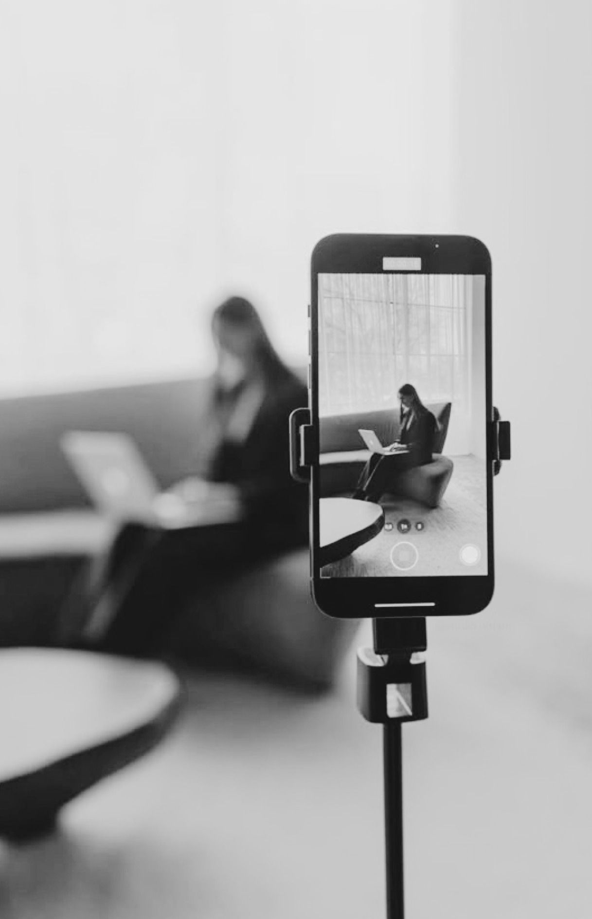 A phone on a tripod framing a shot of a woman working on a laptop